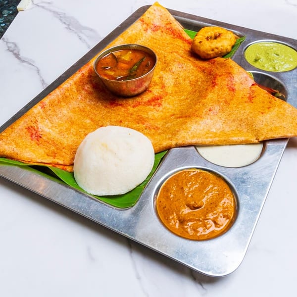 A large dosa, idli, vada, sambar, and three chutneys on a metal tray from Chennai Chettinaad Palace.