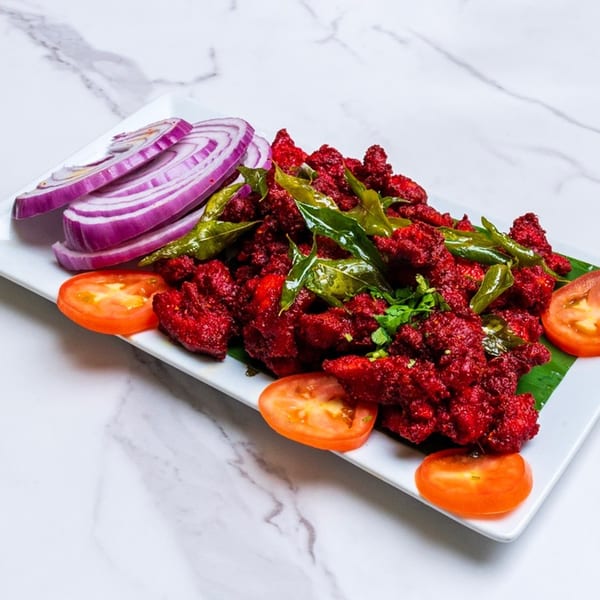 Chennai Chettinaad Palace's bright red chicken dish, garnished with green leaves, red onions, and tomato slices.
