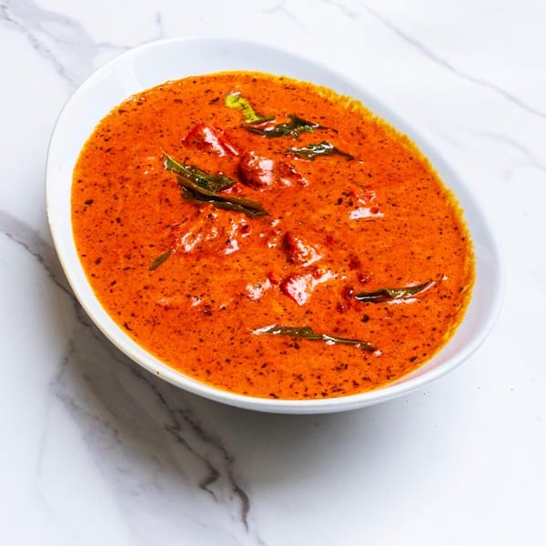 A vibrant orange Indian curry with chicken pieces and green herbs in a white oval bowl.