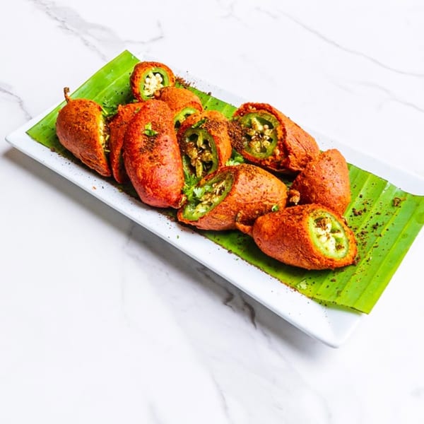 Spicy green chili pakoras, some sliced open, served on a banana leaf on a white plate.