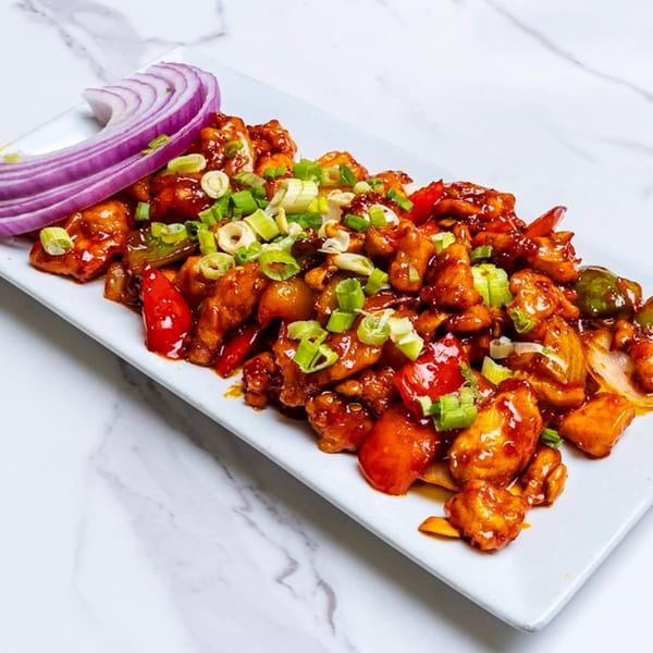 Chennai Chettinaad Palace's chili chicken, garnished with red onion and green onions on a white plate.
