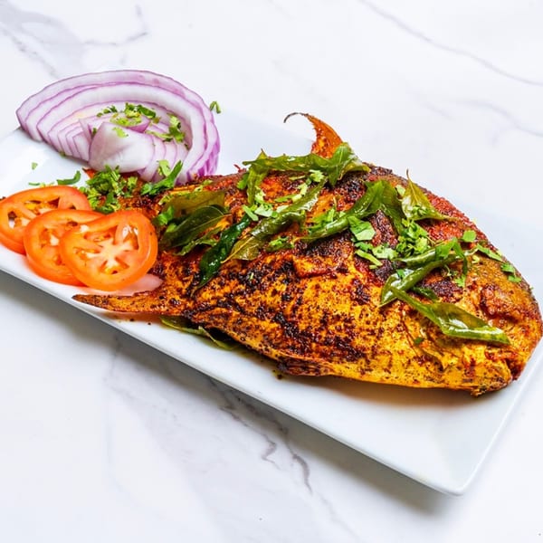 Whole fried fish, garnished with curry leaves, cilantro, sliced tomatoes, and red onions.