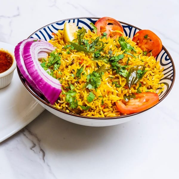 A vibrant bowl of Chennai Chettinaad Palace's biryani, garnished with fresh herbs, lemon, onion, and tomato.