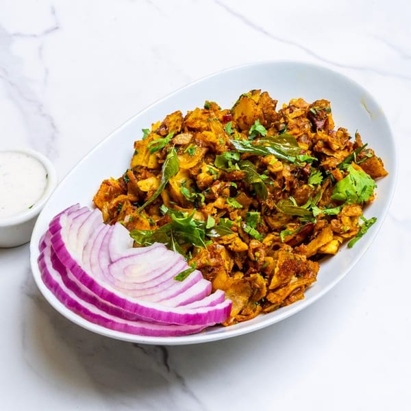 Spicy Indian Chettinad mushroom dish with red onion slices and a side of white sauce.