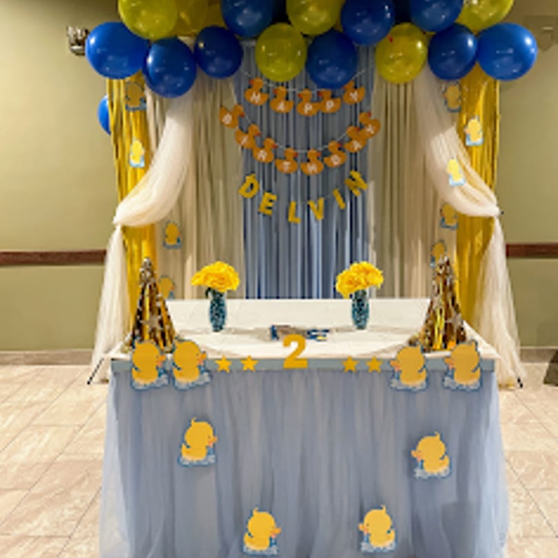 A birthday party setup with blue and yellow balloons, a "Happy Birthday Delvin" banner, and a decorated table.